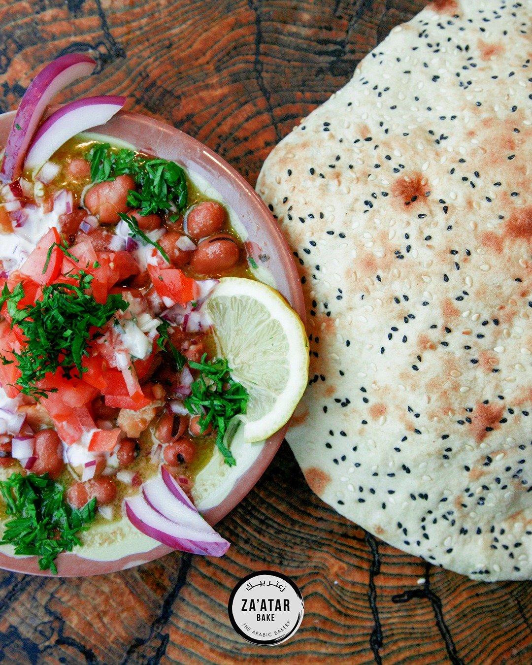 Za'atar Bake ful medames fava bean dip topped with diced tomatoes and herbs, served with fresh sesame flatbread